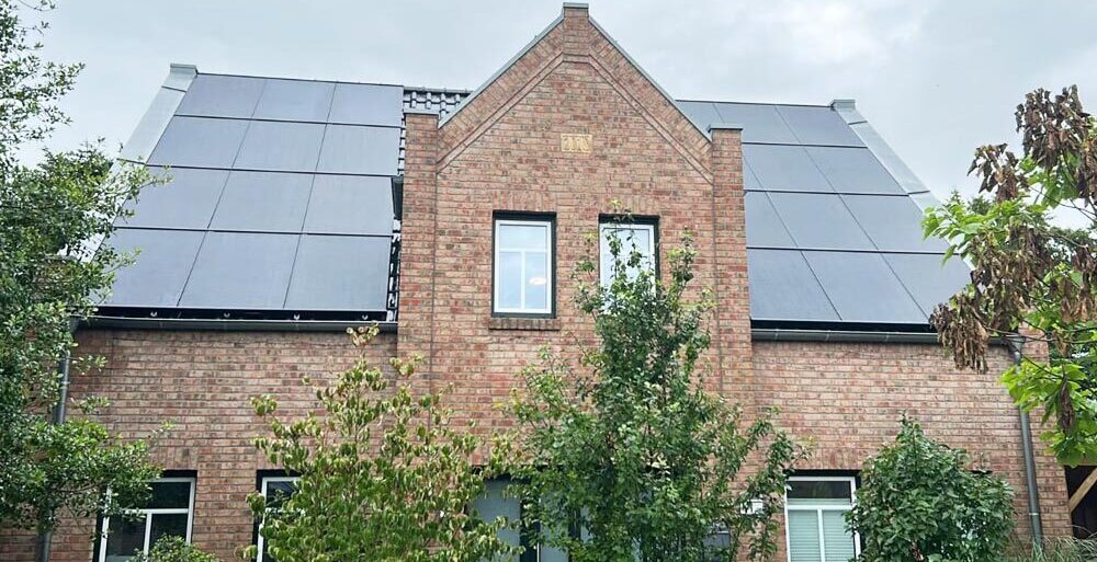 Backsteinhaus mit großen Solarmodulen auf beiden Dachseiten, umgeben von Bäumen.